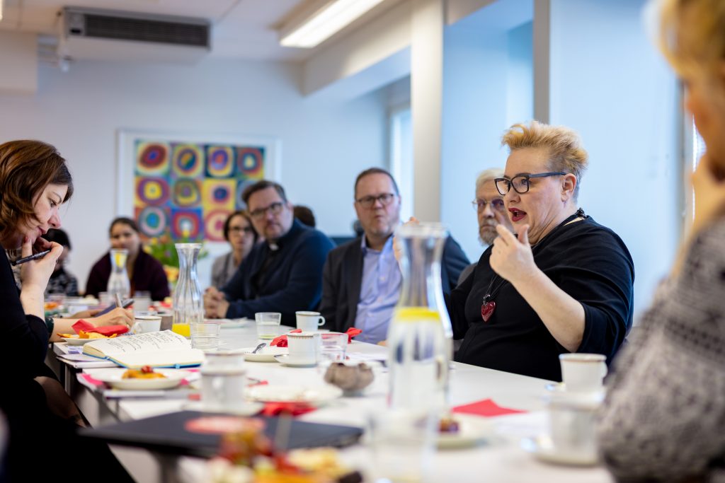 Ihmisiä keskustelemassa pöydän ympärillä.Keskellä kuvassa europarlamentaarikko Sirpa pietikäinen.