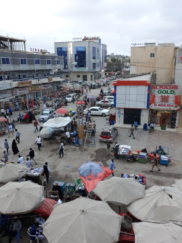 Kaupunkinäkymä; ihmisiä, autoja, liikkeitä, myyntikojuja. Tuulevaisuuden etsijät -hanke toimii Pohjois-Somaliassa.