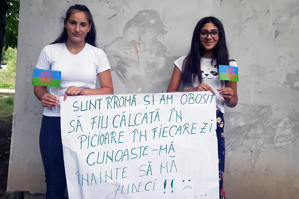 Två flickor med en skylt. Skylten har en rumänsk text.