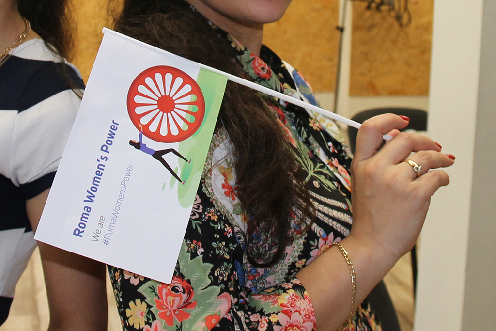 Nuoren romaninaisen kädessä viiri, jossa lukee Roma Women's Power. Valko-Venäjä on hänen kotimaansa.