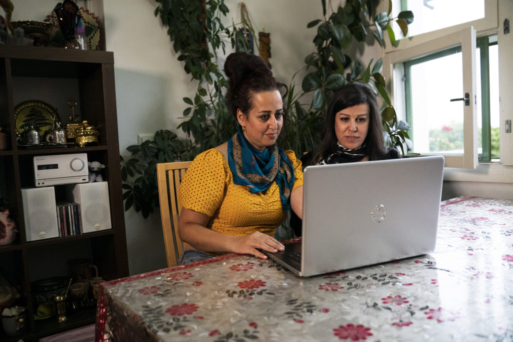 Kaksi naista istuvat pöydän ääressä tietokoneella työskennellen. Maahanmuuttajien työllistyminen on heille yhteinen aihe.