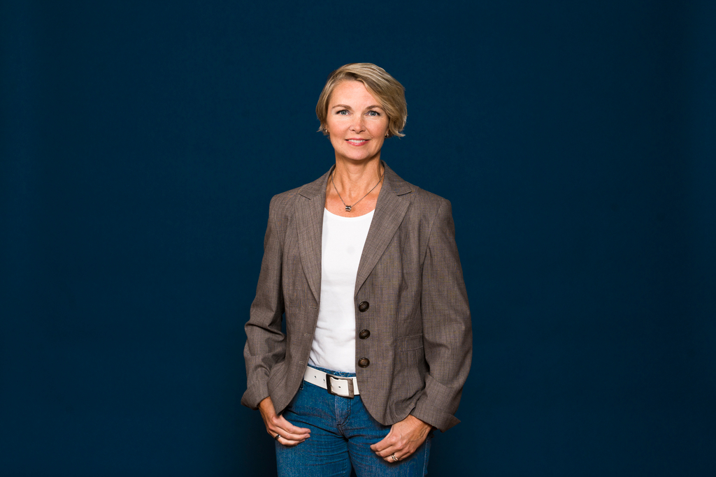 Nina Leppäkangas seisoo tummansinisen taustan edessä kameraan katsoen.