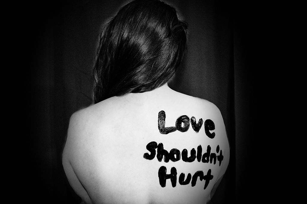 A woman with a text "Love shouldn't hurt" written on her back