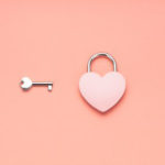 Vaaleanpunaisella taustalla avain ja sydämenmuotoinen lukko.