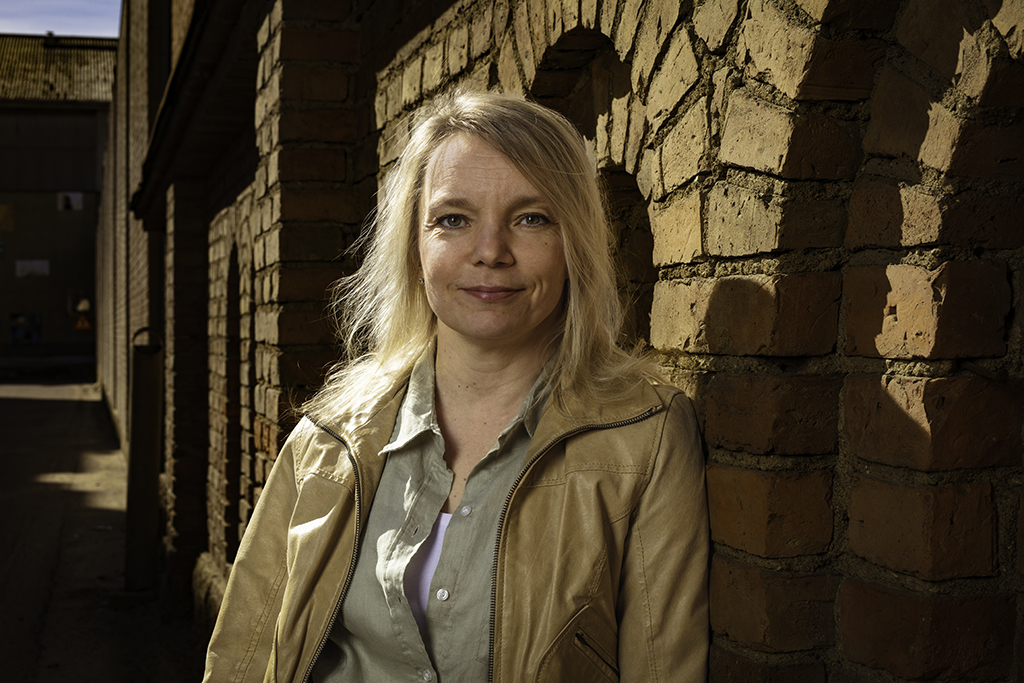 A woman beside a brick wall. Her name is Mari Tikkanen.