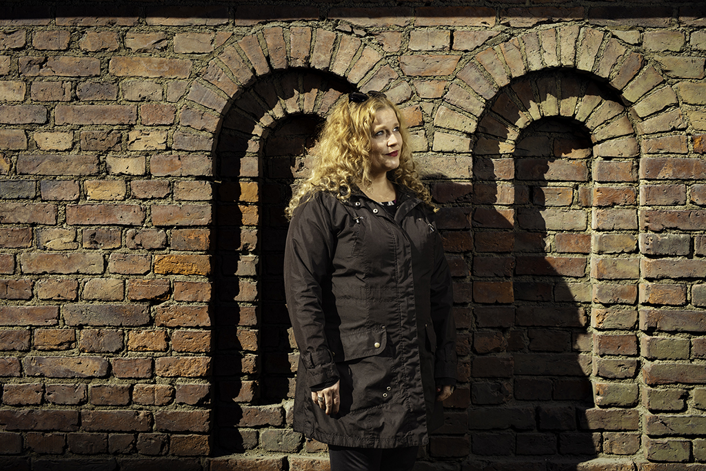 A woman beside a brickwall. Her name is Marjo Neste.