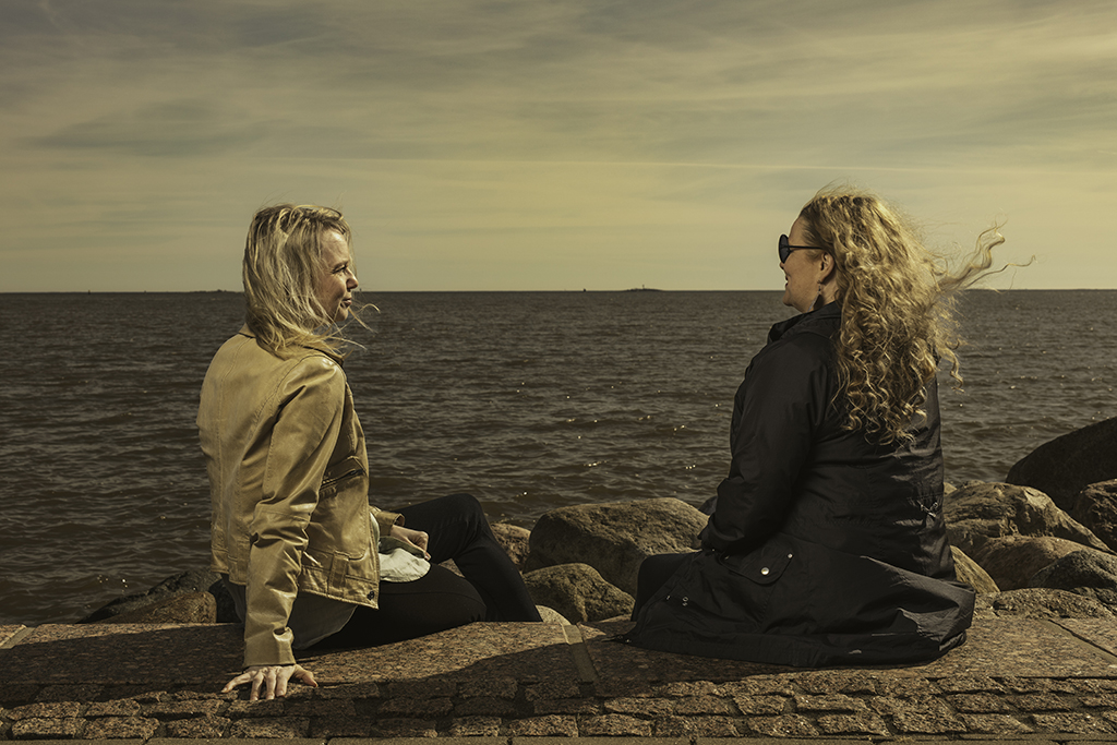 kaksi naista istuvat meren ääressä.
