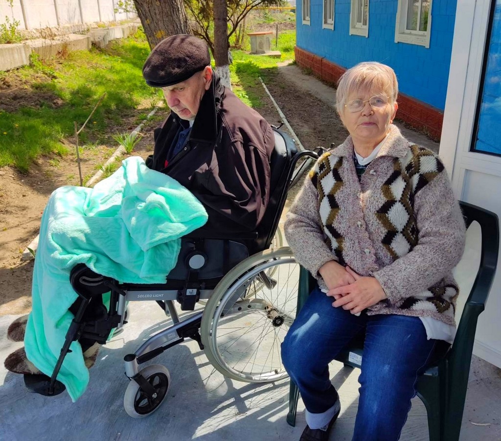 Pyörätuolissa istuva mies ja hänen avustajansa istuvat Greblestin pakolaiskeskuksen edustalla.