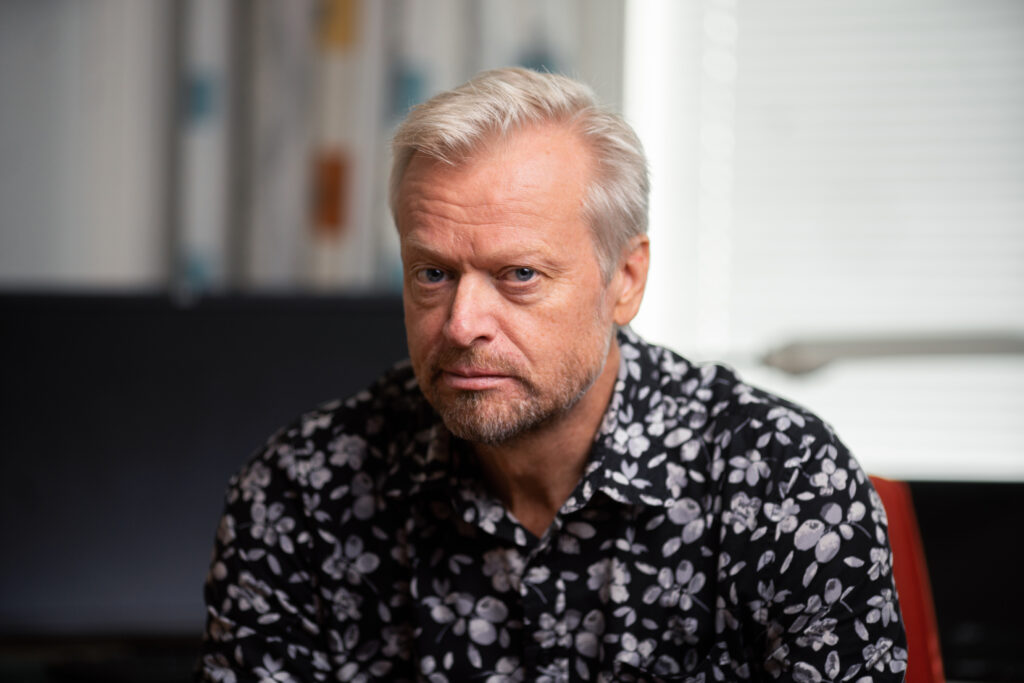 Vaaleahiuksinen mies katsoo kameraan puolilähikuvassa.
