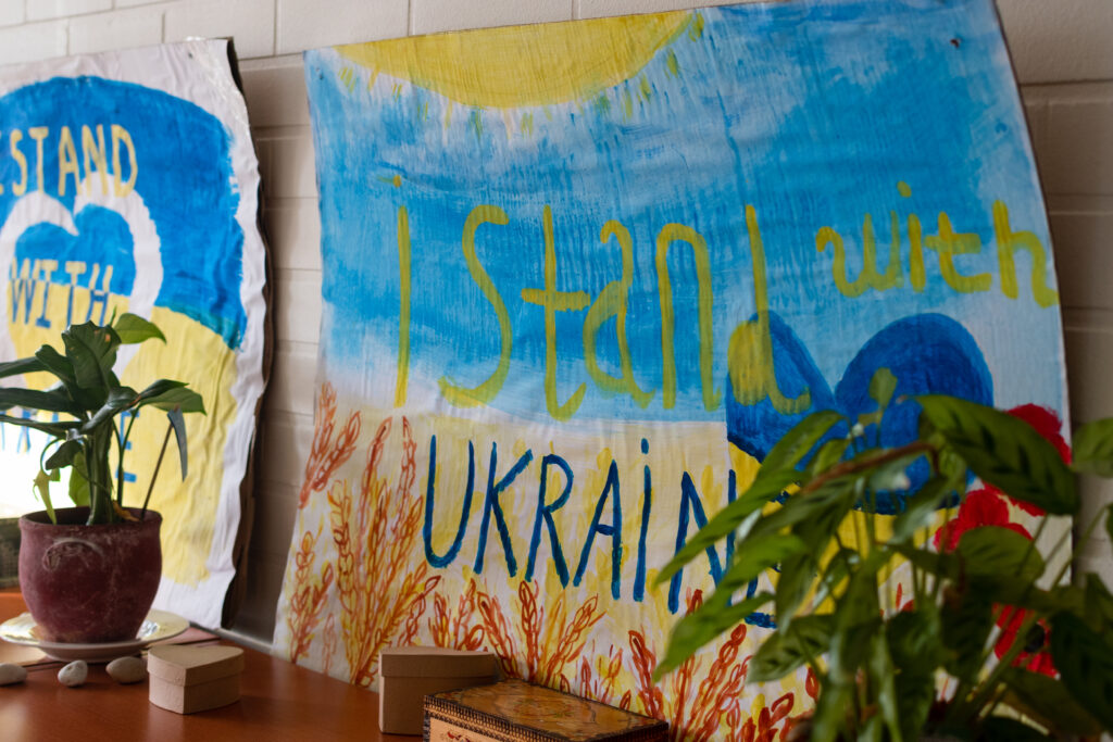 Sinikeltainen maalaus, jossa teksti "I stand with Ukraine". 