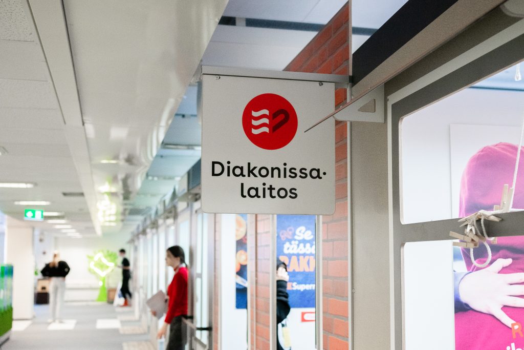 Eri yritysten toimitiloja sisältävän käytävän varrella kyltti, jossa lukee Diakonissalaitos.