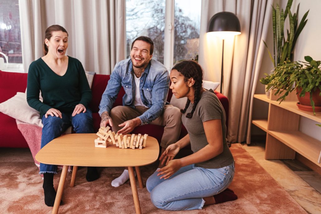 Kolme nuorta henkilöä istuu pöydän ääressä pelaamassa Huojuva torni -peliä.