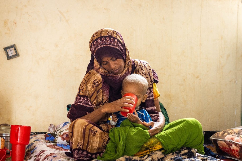 Nainen juottaa sylissään istuvaa pientä lasta.