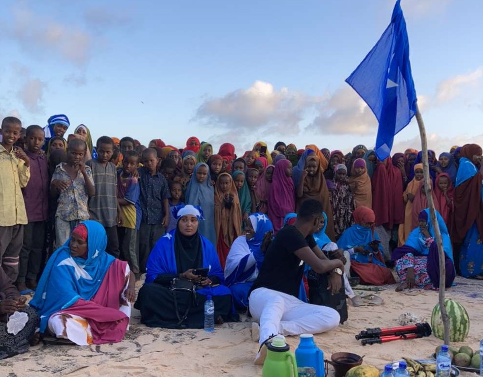 Ryhmä nuoria on kokoontunut yhteen Somalian lipun ja maassa hiekassa olevien tarjoilujen ääreen.