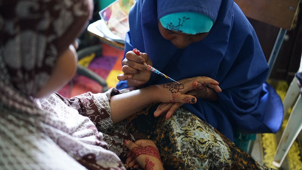 A young woman is making henna ornaments on another young woman's hand.