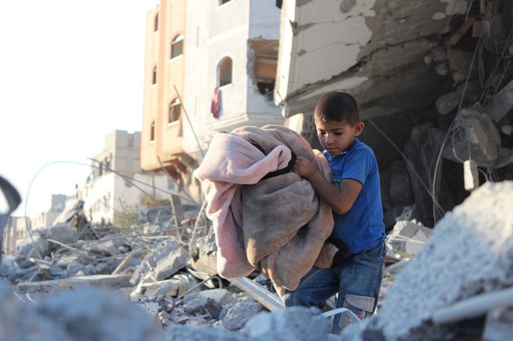 Poika kantaa tavaroita raunioiden keskellä. Gaza on taistelujen kohteena.