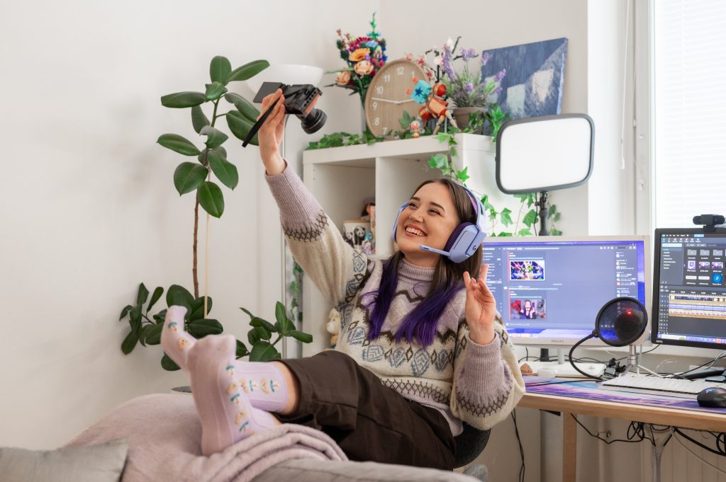 Nuori nainen istuu tietokonepöydän ääressä ja kuvaa itseään videokameralla.