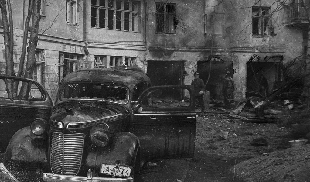Auto ja rakennus, jotka ovat vaurioituneet pommituksessa. Sota-aika teki tuhoa.
