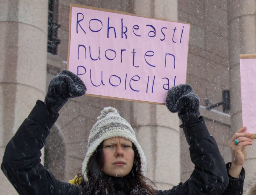 Esther Grönstrand pitämässä kylttiä päänsä yläpuolella jossa lukee "Rohkeasti nuorten puolella!"