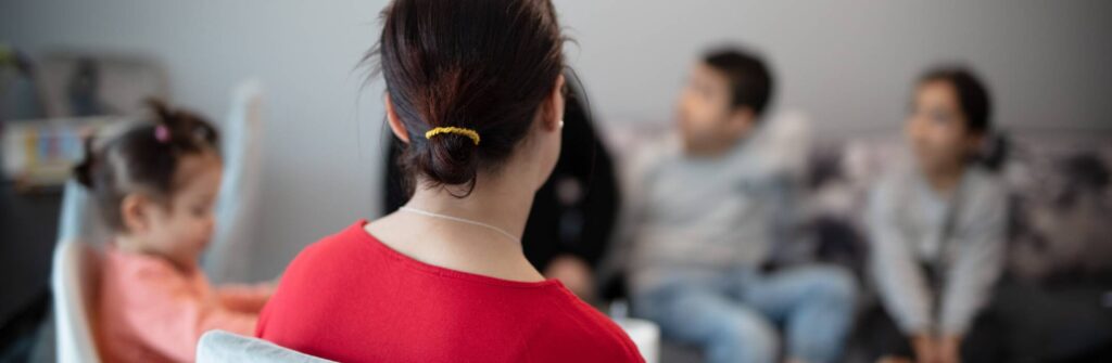 Nainen kuvattuna takaapäin. Taustalla lapsia.