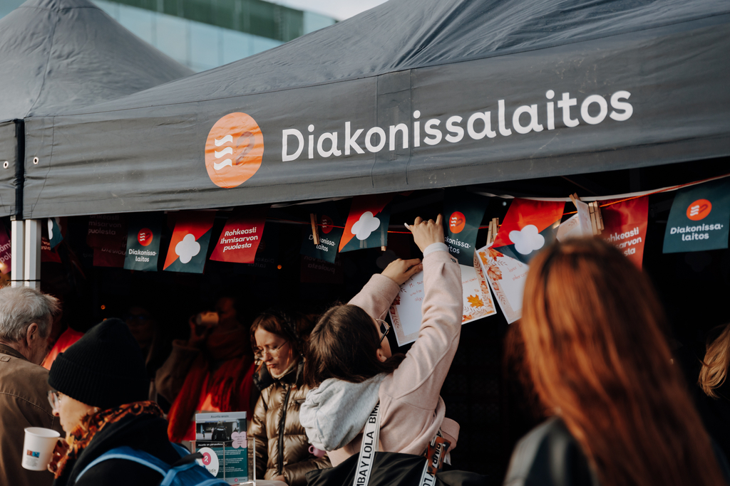 Ihmisiä Diakonissalaitoksen teltan edessä kiinnittämässä kortteja narulle. 
