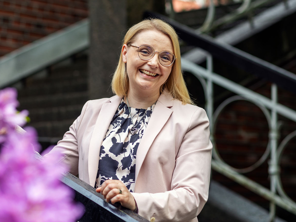 Vaaleaan bleiseriin pukeutunut nainen katsoo hymyillen kameraan.