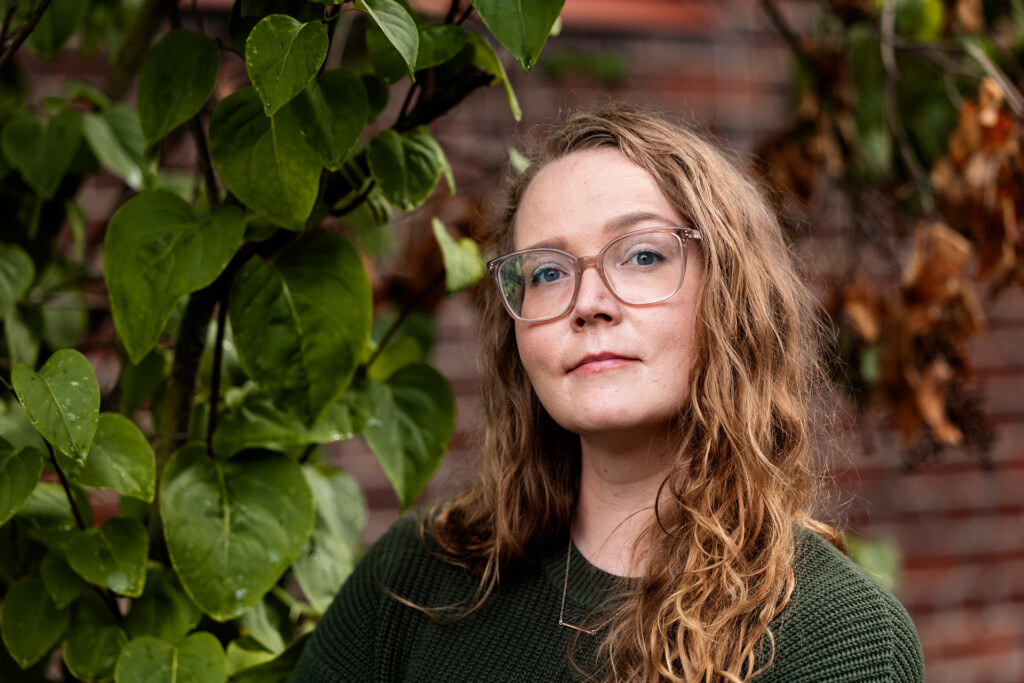 Vihreään villapaitaan pukeutunut, silmälasipäinen ja ruskeahiuksinen nainen katsoo hymyillen kameraan.