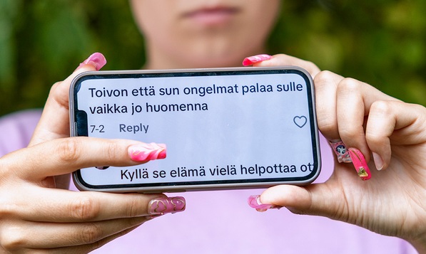 Nuori pitää puhelinta esillä. Ruudussa näkyy ikäviä kommentteja.