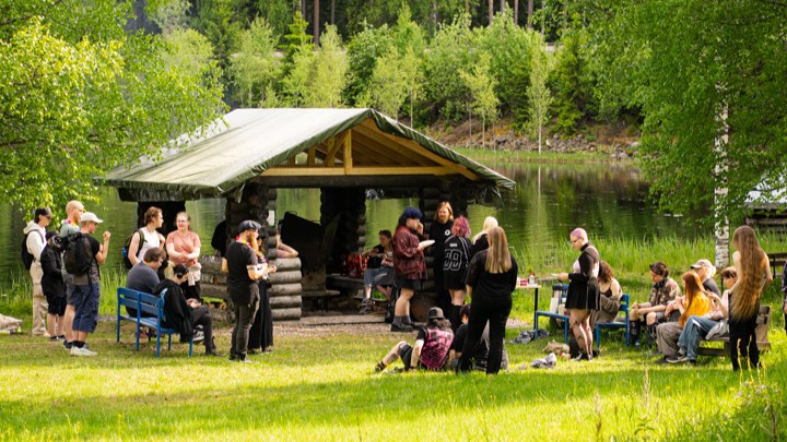 Joukko nuoria viettää aikaa kesäisessä maisemassa järven rannalla.