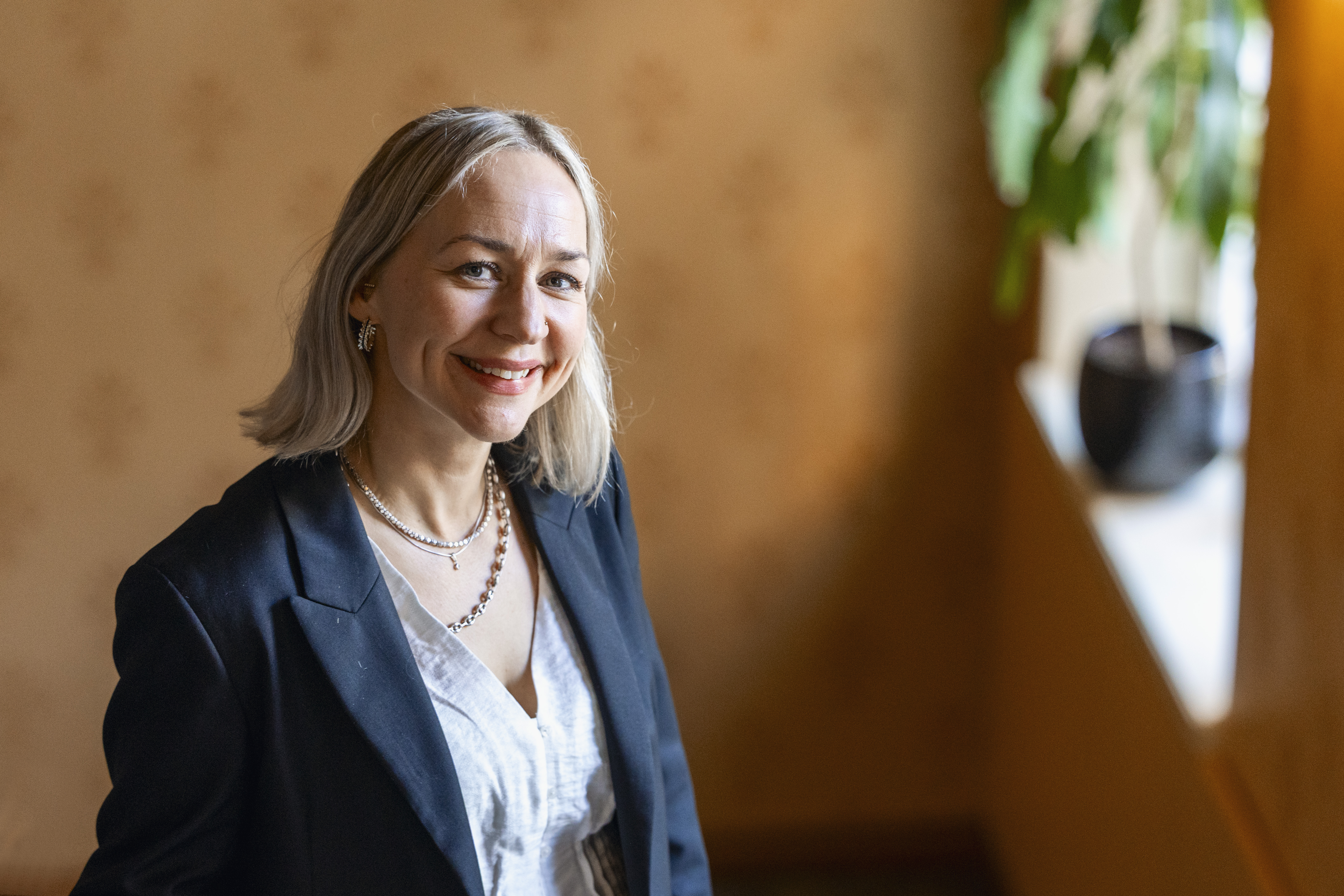 Mustaan jakkupukuun pukeutunut vaaleahiuksinen nainen katsoo hymyillen kameraan.