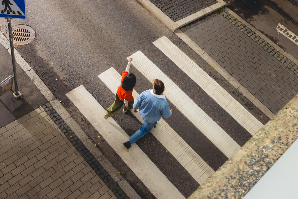 Kaksi henkilöä ylittää suojatietä, ja toinen osoittaa kädellä eteenpäin.
