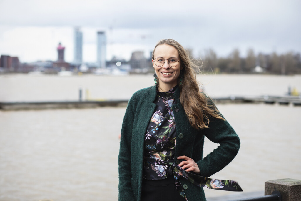 Nainen seisoo merenrannassa ja hymyilee.