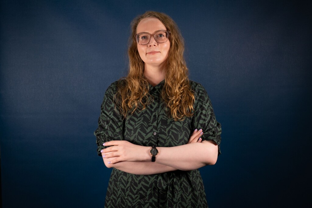 Ruskeahiuksinen nainen katsoo hymyillen kameraan.