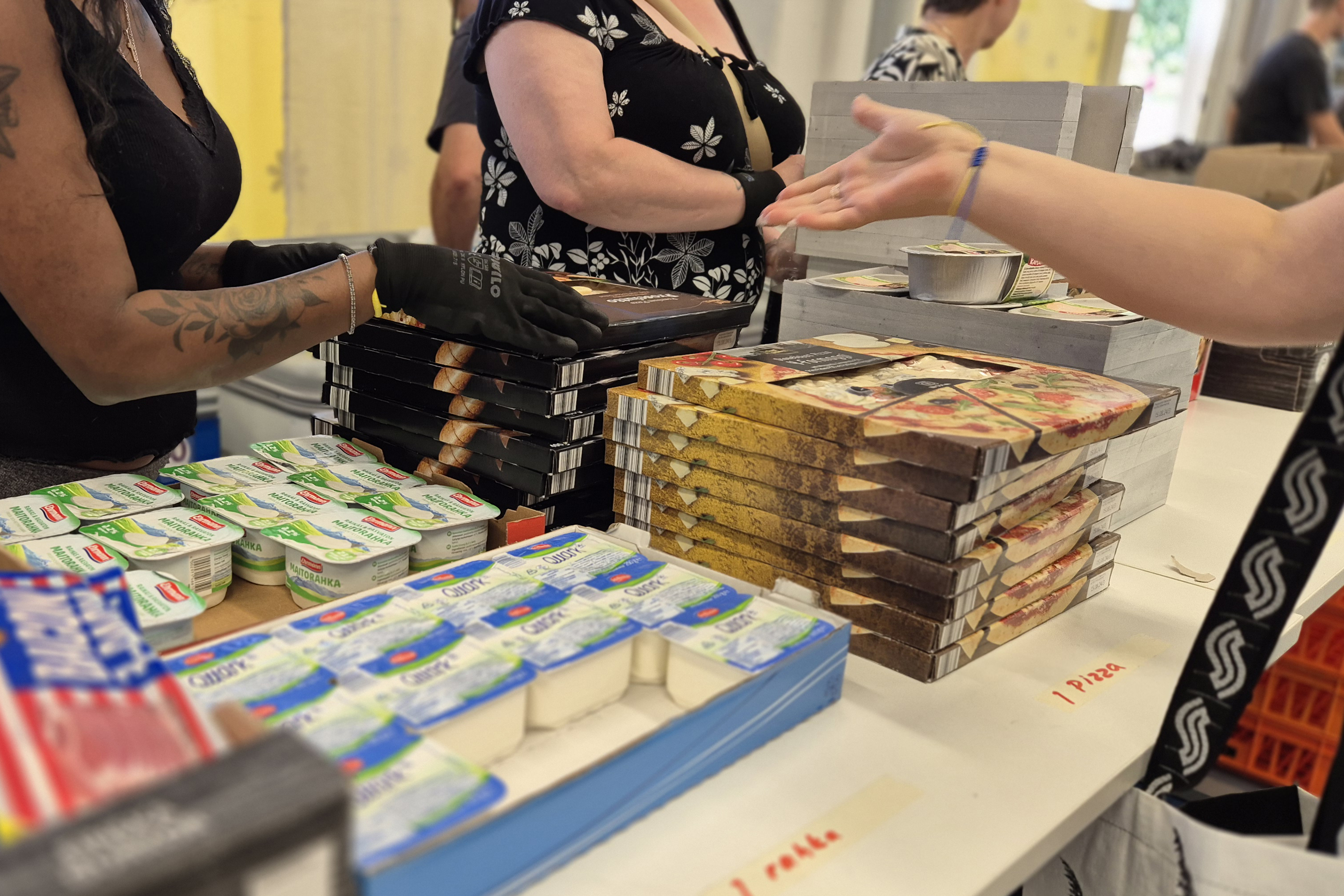 Ruoka-apujonossa työntekijä on ottamassa pizzalaatikon pinosta ojentaakseen sen asiakkaalle, joka ojentaa kättään työntekijää kohti.