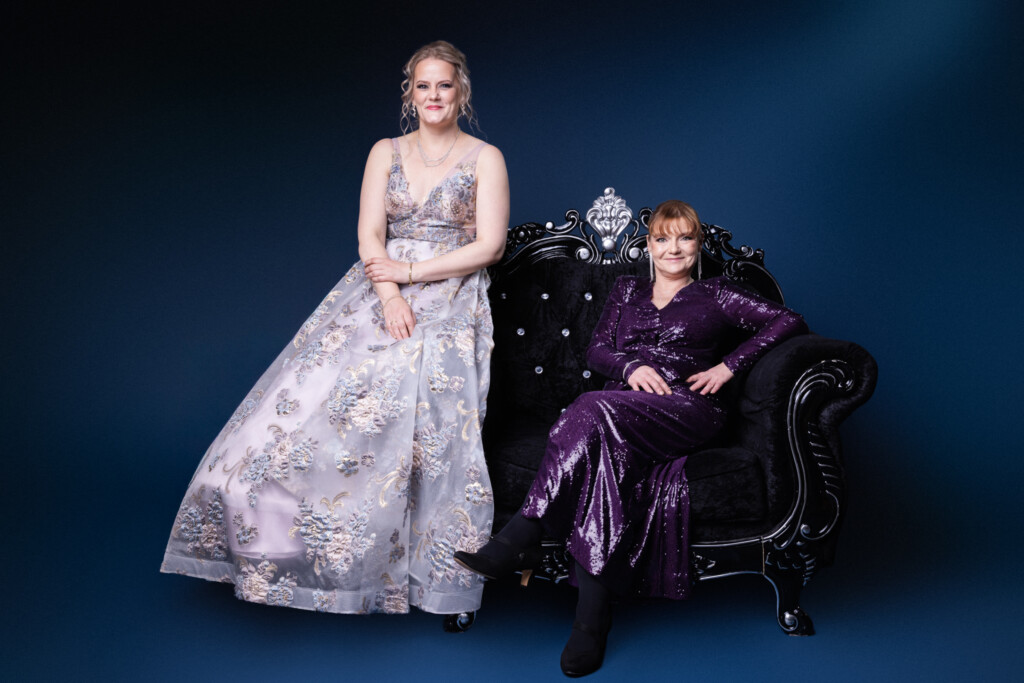 Kaksi naista istuu rinnakkain koristeellisella sohvalla.