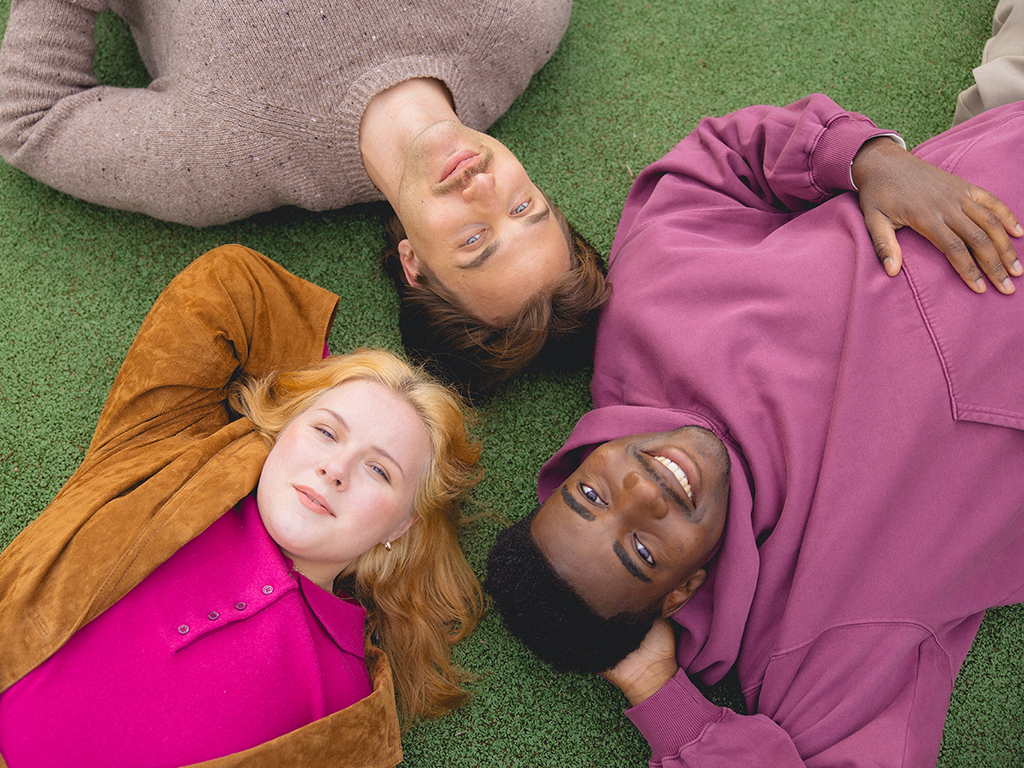 Kolme nuorta makaa viheriöllä hymyillen.